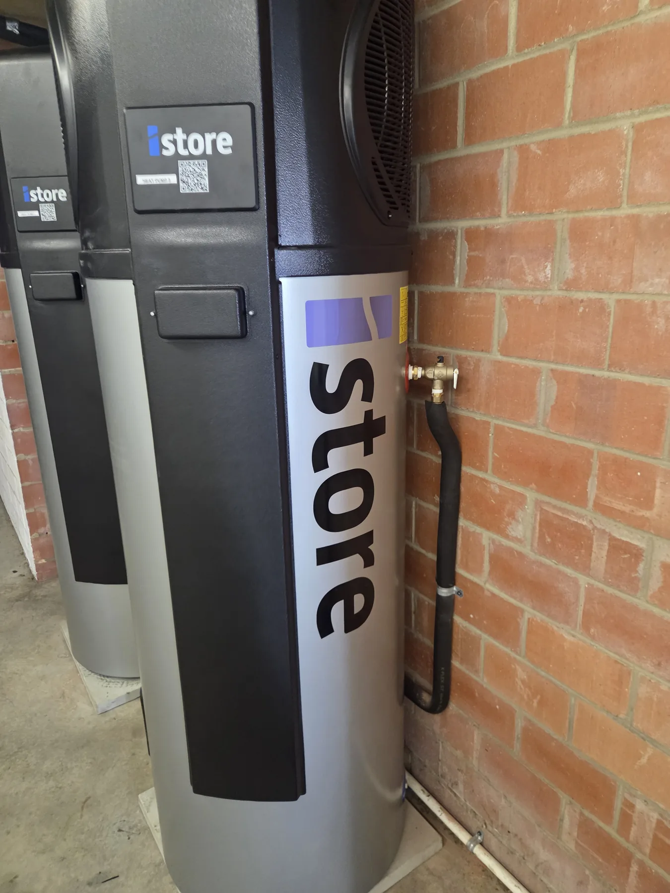 Two iStore heat pump hot water systems installed beside a brick wall by Unisol